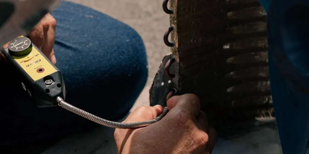 Close-up of hands working to clean AC condenser coils and the metal fins outdoors