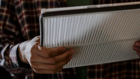 Homeowner holding a pleated HVAC air filter while diagnosing why the house gets so dusty