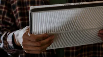 Homeowner holding a pleated HVAC air filter while diagnosing why the house gets so dusty