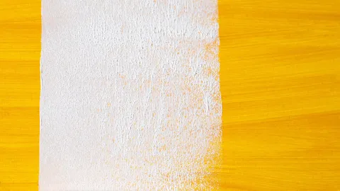 Paint roller laying a white stripe over a dark surface, painting over dark walls