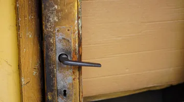 Close-up of a wooden door handle and latch plate, fixing a door that won't close