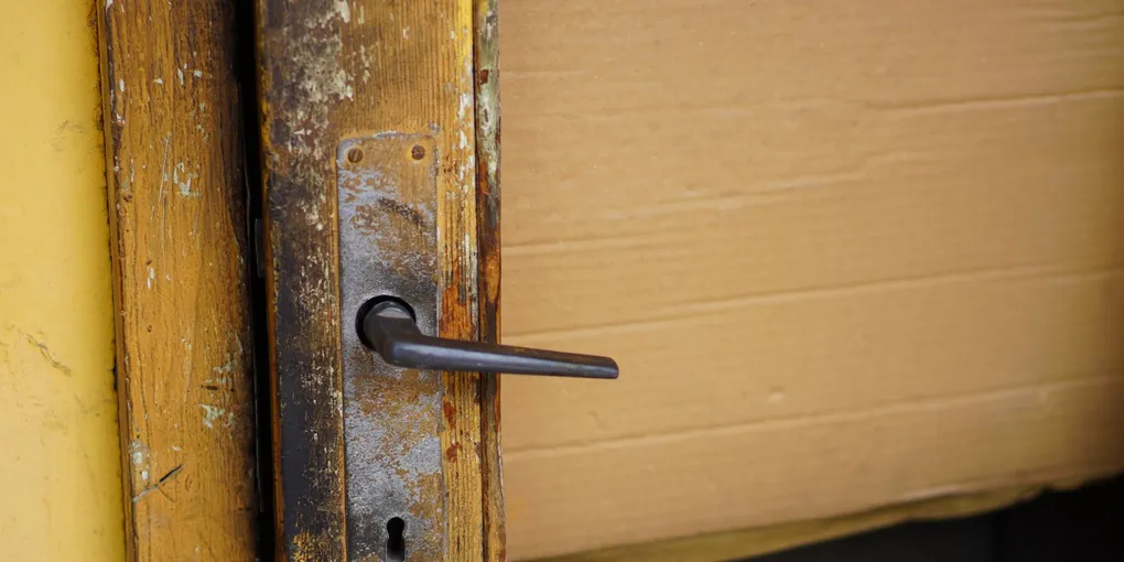 Close-up of a wooden door handle and latch plate, fixing a door that won't close