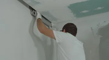 Person finishing an interior drywall seam with joint compound to fix a crack in drywall