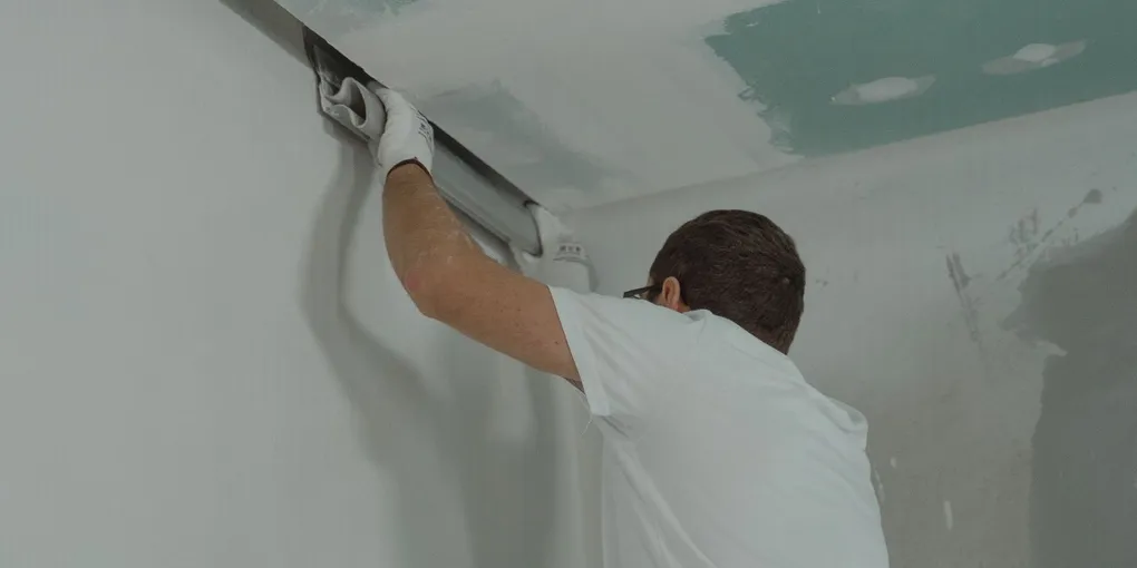Person finishing an interior drywall seam with joint compound to fix a crack in drywall