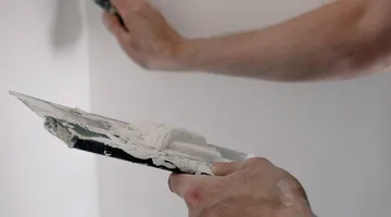 Hands spreading joint compound on a wall with putty knives, how to patch a hole in drywall