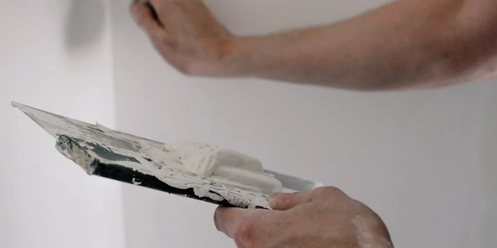 Hands spreading joint compound on a wall with putty knives, how to patch a hole in drywall