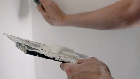 Hands spreading joint compound on a wall with putty knives, how to patch a hole in drywall
