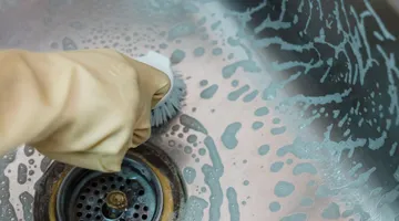 Gloved hand clearing a kitchen sink drain opening, how to fix a garbage disposal that hums