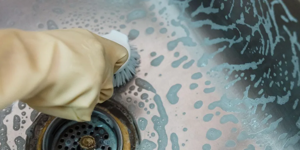 Gloved hand clearing a kitchen sink drain opening, how to fix a garbage disposal that hums
