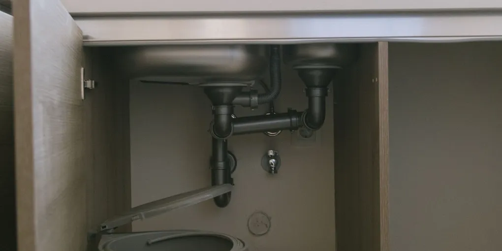 Open under-sink cabinet showing drain plumbing where a garbage disposal can leak from the bottom
