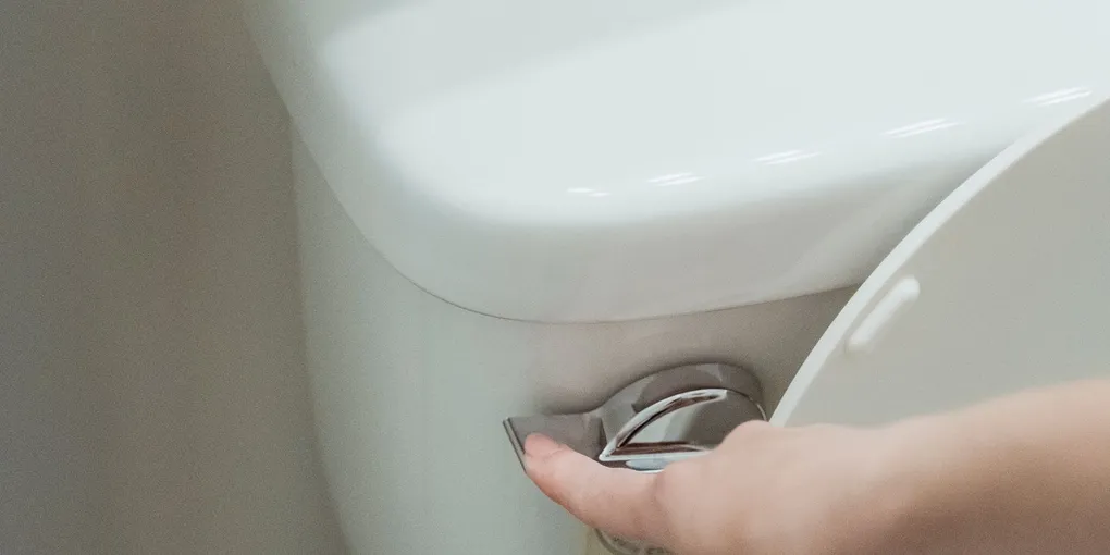 Hand pressing the flush lever on a white residential toilet that keeps gurgling