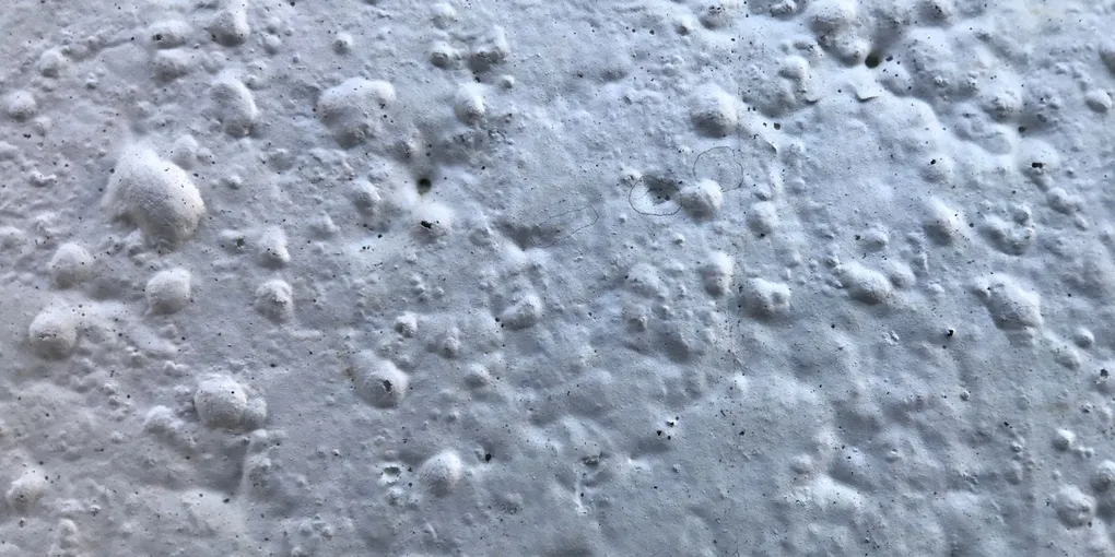 Close-up of a white wall showing raised rounded blisters, bubbles in drywall paint