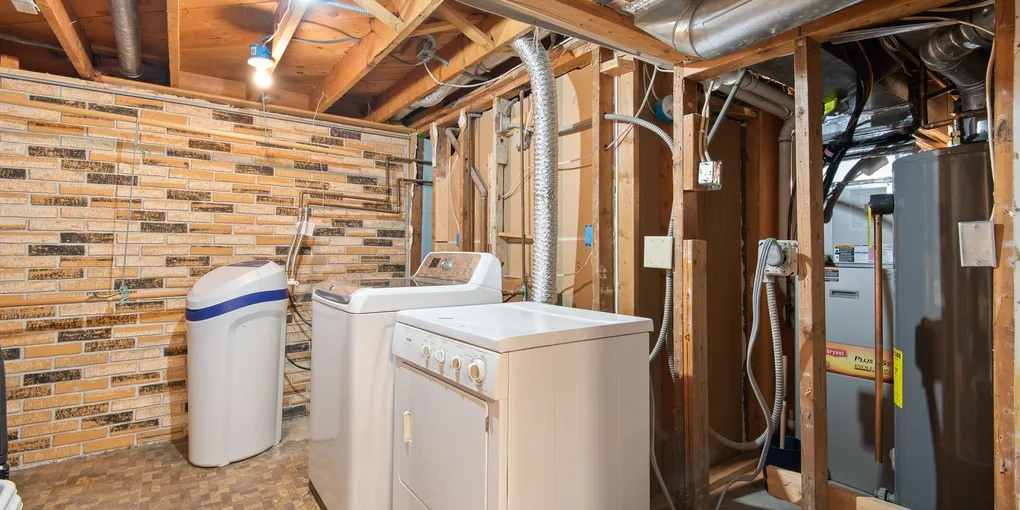 Floor-standing water heater tank in a basement utility area with a leak at the base