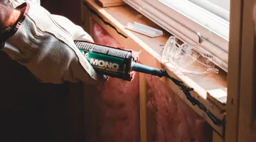 Gloved hand sealing a window frame gap to weatherstrip windows against summer air leaks