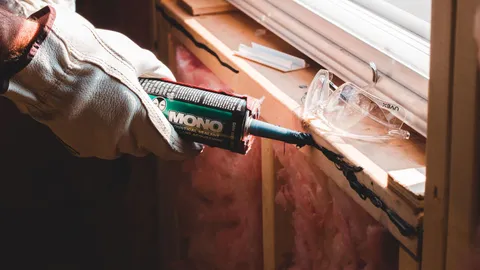 Gloved hand sealing a window frame gap to weatherstrip windows against summer air leaks